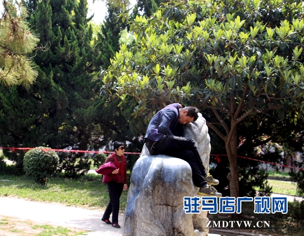 儿童公园内，一男子坐在石兽上玩手机.JPG